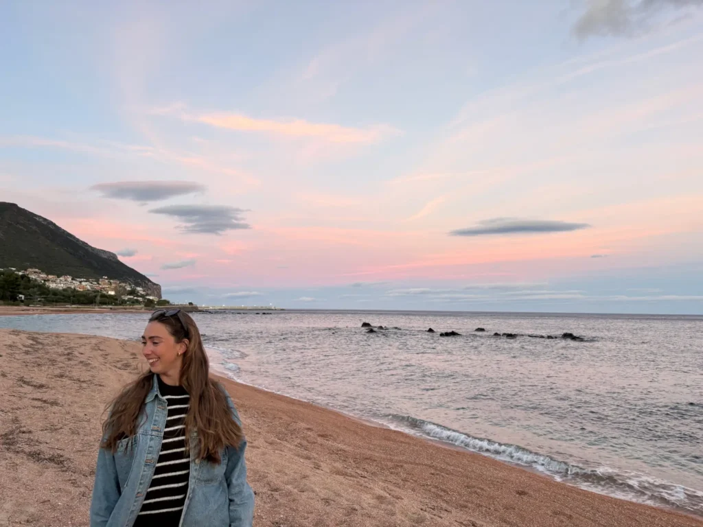 Junge Frau lächelt an einem ruhigen Strand mit pastellfarbenem Abendhimmel und Meerblick