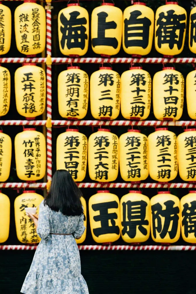 Junge Frau von hinten vor einer Wand traditioneller gelber japanischer Laternen mit Schriftzeichen