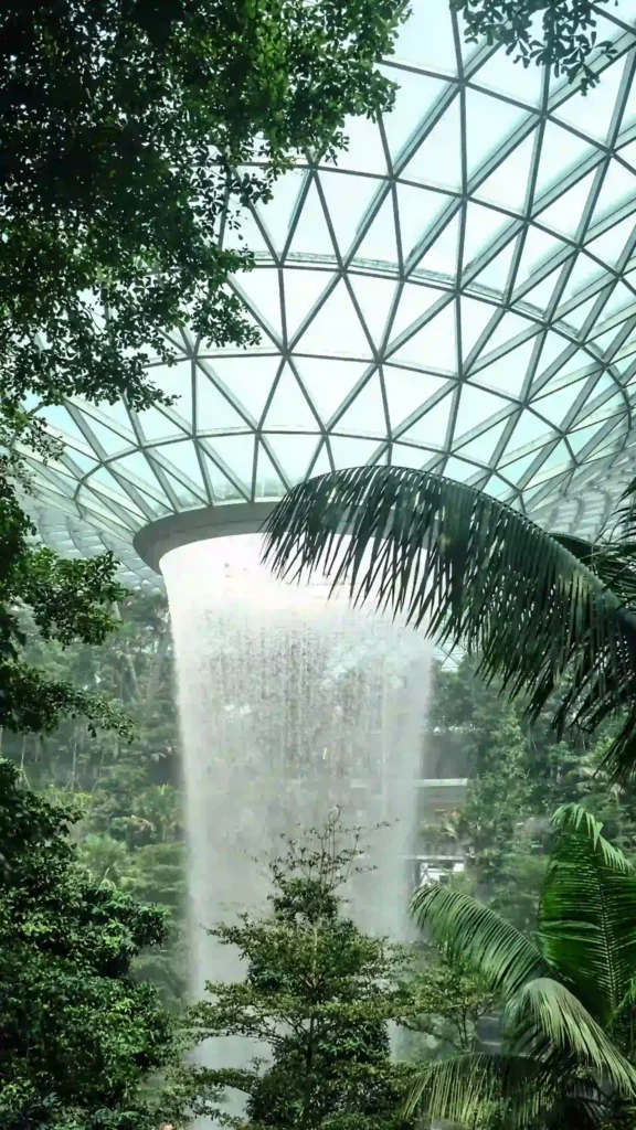 Imposanter Indoor-Wasserfall im Jewel Changi Airport Singapur, umgeben von tropischer Vegetation unter einer gläsernen Kuppel